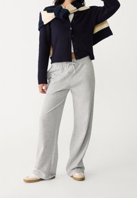 Grijze joggingsbroek met een elastische tailleband en trekkoord, gecombineerd met een marineblauwe cardigan en een lichtgekleurde trui over de schouders.