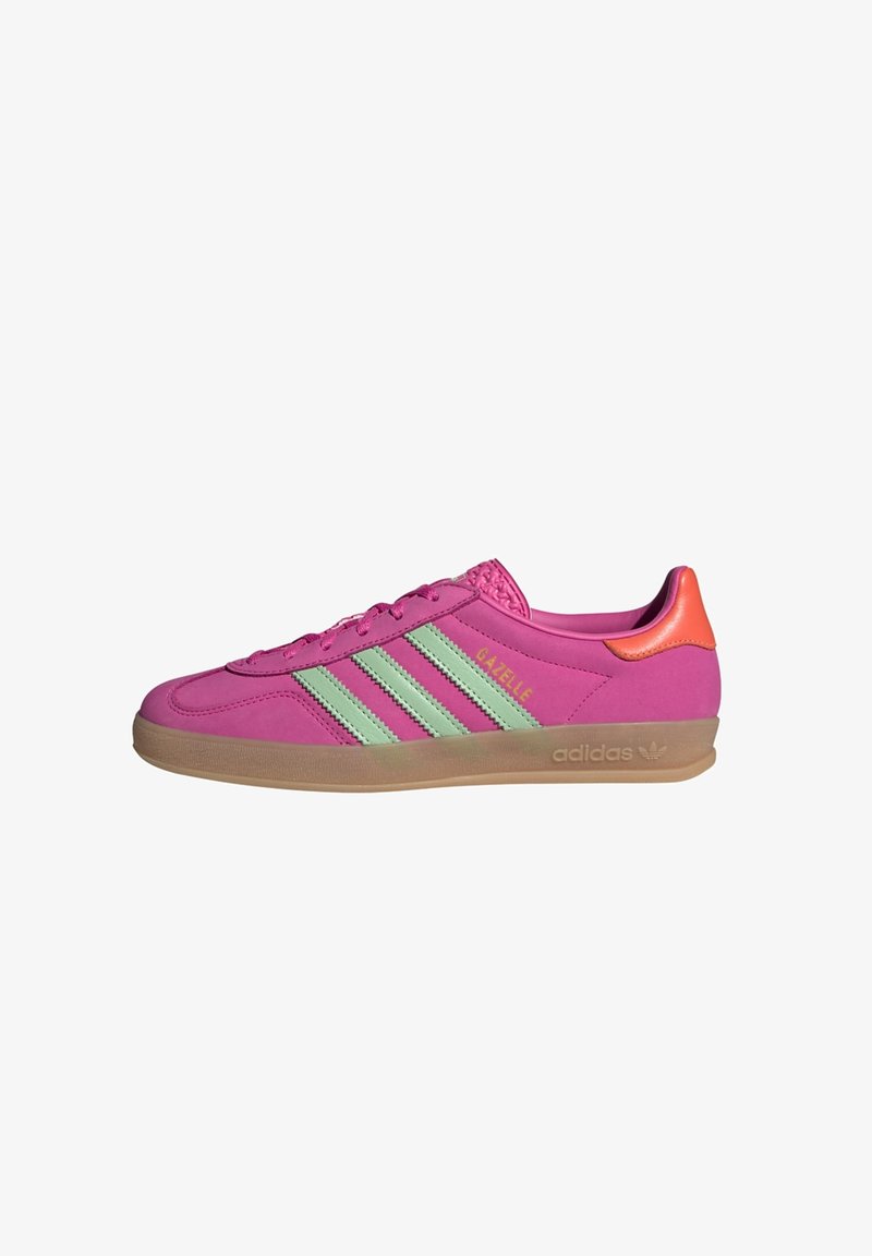 Adidas Gazelle sneakers in bright pink with light green stripes, rubber sole, and orange heel accent. Smooth synthetic upper material.