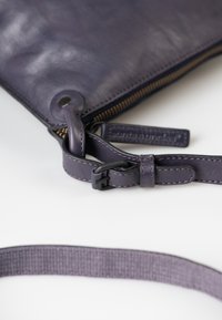 Clutch in pelle viola con chiusura a zip, dotata di un anello circolare e di una tracolla regolabile con un moschettone e cuciture decorative.