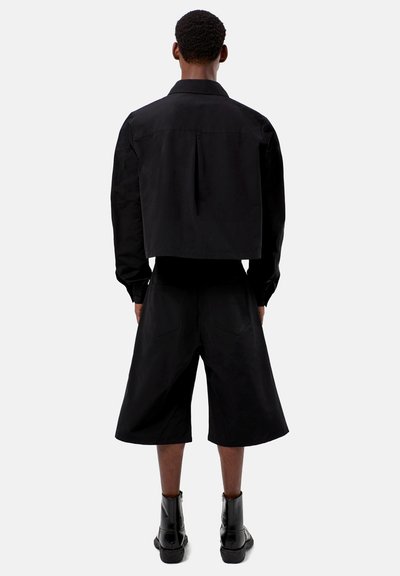 Svart kort jacka med rak skärning, med en bakfälg. Kombinerad med lösa svarta shorts och svarta ankelstövlar.