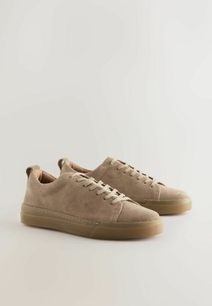 Beige ruskindssneakers med flade snørebånd, lavt snit og gummisål. Har en sømløs tåhætte og syningsdetaljer.