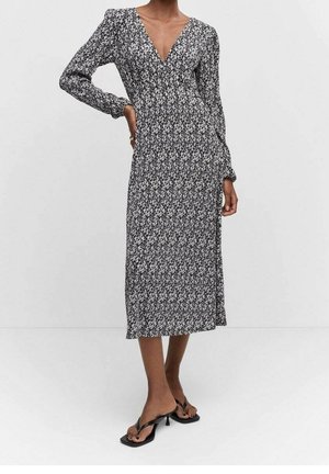 Zwart-witte jurk met bloemenprint, lange mouwen, V-hals, lengte tot halverwege de kuit, zachte stof en een ontspannen pasvorm. Gecombineerd met zwarte sandalen.