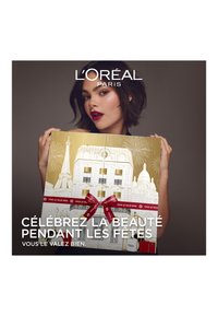 Boîte-cadeau dorée présentant un design de skyline parisien, attachée avec un ruban rouge. Comprend plusieurs petites bouteilles avec la marque L'Oréal Paris.