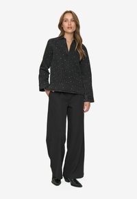 Pull noir avec des éclats en forme d'étoiles, coupe décontractée et col, associé à un pantalon noir ample et des chaussures noires brillantes.