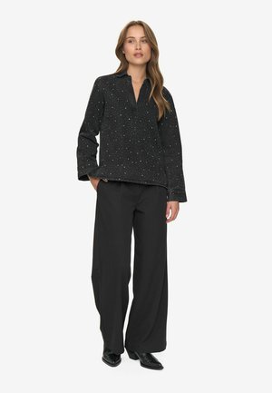 Pull noir avec des éclats en forme d'étoiles, coupe décontractée et col, associé à un pantalon noir ample et des chaussures noires brillantes.