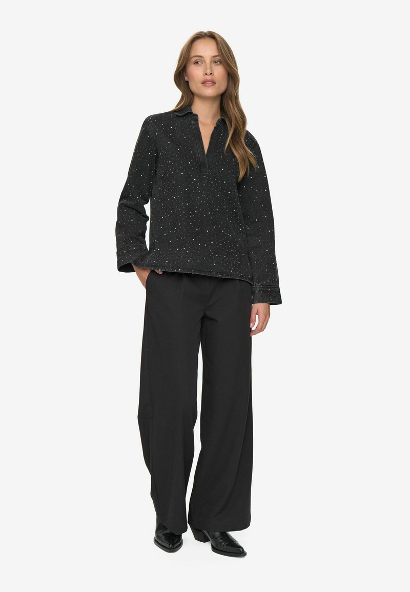 Pull noir avec des éclats en forme d'étoiles, coupe décontractée et col, associé à un pantalon noir ample et des chaussures noires brillantes.