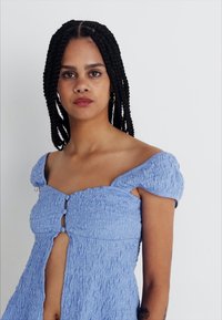 Vaaleansininen mekko, jossa on teksturoitu kangas, joustava olkaimeton muotoilu, napit edessä ja avaus avainreijällä.