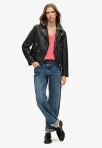 Svart lädermotorcykeljacka med silverdetaljer, rosa V-ringad t-shirt, blå avslappnade jeans och svarta skor med uppvikt mudd.