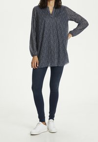 Marine tuniek met een subtiel bloemenpatroon, lange mouwen en een v-hals, gecombineerd met donkere skinny jeans en witte sneakers.