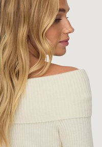 Off-the-shoulder, ribbed sweater in cream, featuring a textured knit pattern with a cozy appearance and soft fabric.