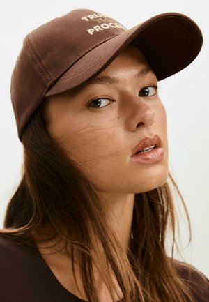 Casquette de baseball marron avec une visière incurvée et le texte "FAIS CONFIANCE AU PROCESSUS". Présente des détails de couture subtils et une texture de tissu lisse.