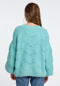 Türkiser, gestrickter Pullover mit einem strukturierten Design, das ein gewelltes Muster aufweist und einen lockeren Schnitt hat, ergänzt durch einen gerippten Saum.