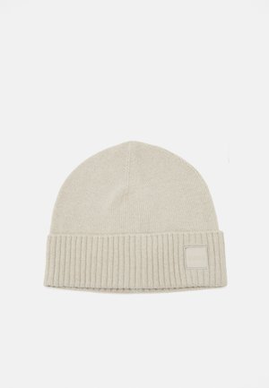 Lichtbeige gebreide beanie met een omgevouwen ribbelmanchet en een klein vierkant logo-label. Zachte textuur en eenvoudig, rond design.