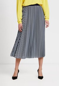 Gonna midi a plissé con righe bianche e nere, dotata di una vita attillata e un design fluido, abbinata a una maglietta gialla brillante.