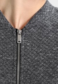 Grijze textuurjacket met een ruitpatroon, voorzien van een metalen rits en een staande kraag, geschikt voor casual wear.