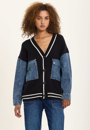 Black and denim cardigan with a V-neck, white accent stripes, button closures, and two front pockets. Soft knit material with a relaxed fit.
