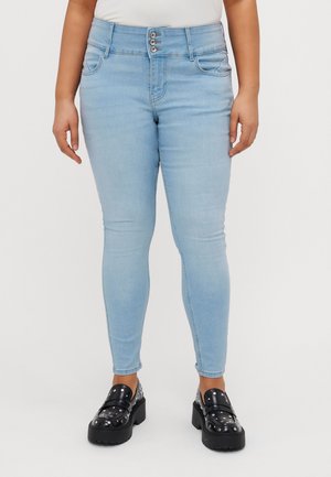 Vrouw draagt lichtblauwe skinny jeans met drie knopen en zwarte gestudeerde plateau loafers.