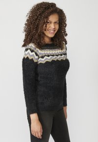 Pull en laine noir et duveteux avec un col rond, orné d'un motif en zigzag blanc, gris et doré sur le col. Un jean noir complète le look.