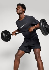 Svart Nike treningsskjorte med hvitt logo, parret med sorte shorts. Personen holder en vektstang med runde vekter.