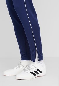 Vita idrottsskor med svarta ränder, som bärs med vita strumpor och marinblå byxor med en vit sidrand och ankelsdragkedja.