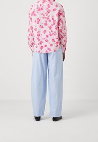 Camicia a bottoni con stampa floreale in rosa con dettagli verdi, abbinata a pantaloni larghi a righe blu chiaro. Scarpe nere completano il look.