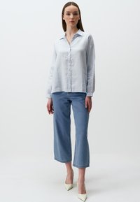 Helles blaues Leinenhemd mit langen Ärmeln, kombiniert mit blauen Caprihosen und cremefarbenen spitzen High Heels. Minimalistisches Design.