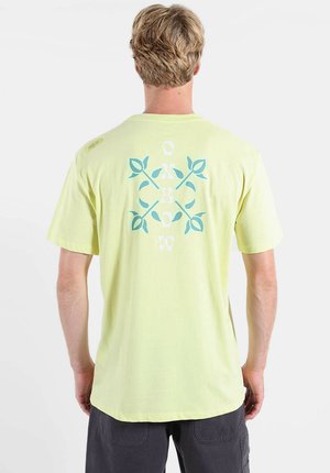 T-shirt en coton jaune clair avec un motif de feuilles et le texte "OKBOW" au dos. Manches courtes avec un accent sur l'épaule.