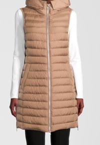 Chaleco acolchado beige con capucha, que presenta un cierre de cremallera frontal completo, textura acolchada, bolsillos laterales y mangas largas en blanco de contraste por debajo.