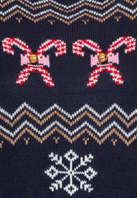 Pull en maille marine avec motifs rouge et blanc de cannes en sucre d'orge, orné de nœuds roses et de clochettes, agrémenté de dessins en zigzag dorés et blancs, et d'un flocon de neige.