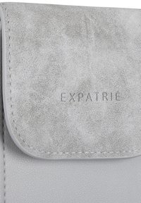 Borsa in pelle sintetica grigia con superficie texturizzata, dotata di chiusura a pattina e logo "EXPATRIÉ" embossato sulla parte anteriore.
