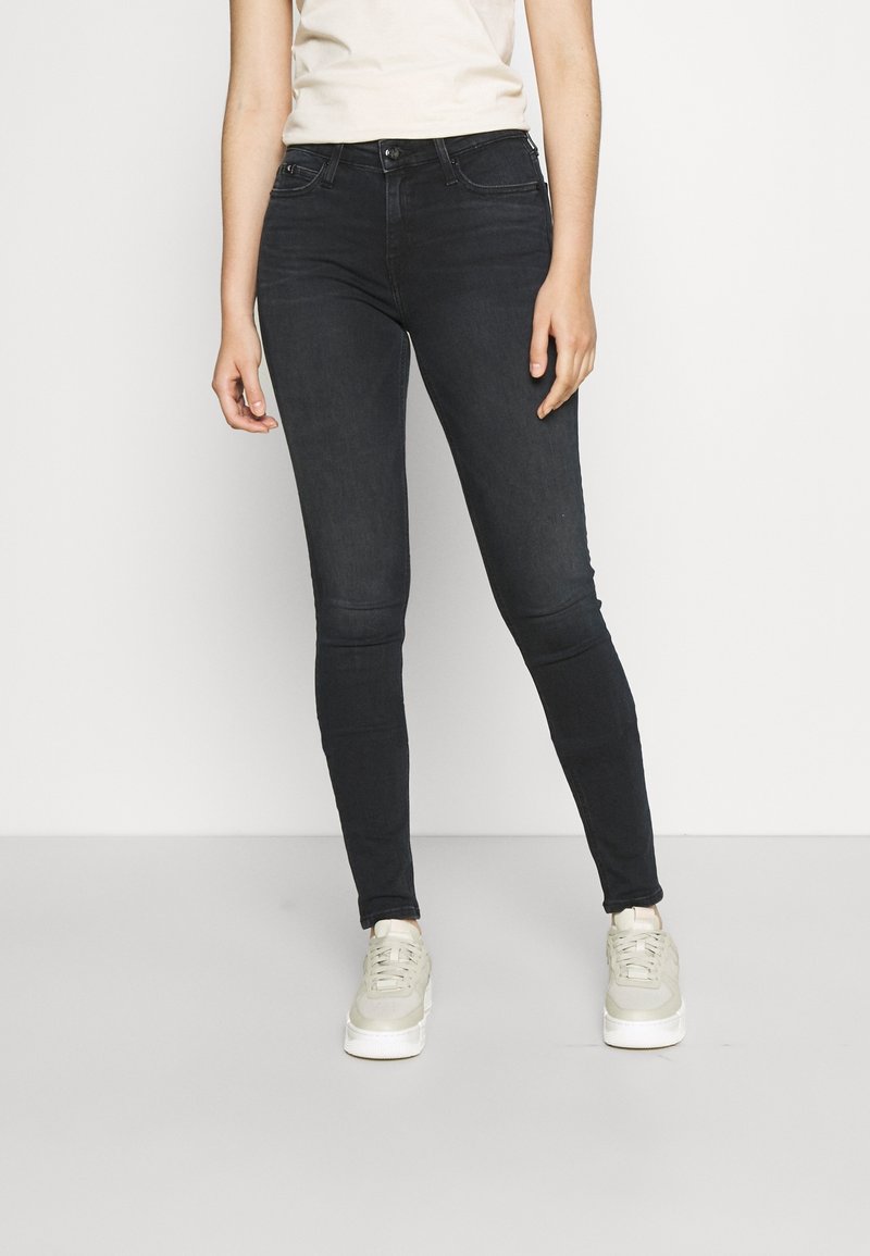 Jeans ajustados en lavado oscuro, con una cintura alta, diseño de cinco bolsillos y costuras sutiles. Combinados con zapatillas casuales de color claro.