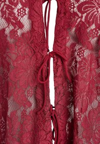 Bordeauxblondert tøj med blomstermønstre og en snørelukning foran. Stoffet har en delikat, semitransparent tekstur.