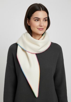 Woman with straight dark hair wears a white triangular scarf with multicolor stitching over a dark gray ribbed sweater.