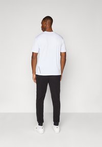 Witte T-shirt met korte mouwen en een ronde halslijn, gecombineerd met zwarte tapered broek en witte sneakers, met ritszakken aan de zijkant.