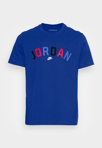 Camiseta azul de manga corta con el texto "JORDAN" en multicolor y el logo de la marca Nike en blanco centrado bajo el texto.