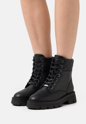 Zwarte veterschoenen tot de enkel met doorgestikte accenten, een platte dikke zool en een ronde neus. Gemaakt van glad leer met zilverkleurige metalen details.