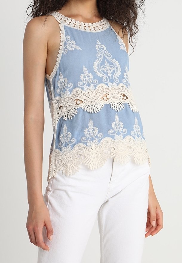 Blå ärmlös topp med intrikata vita spetsdetaljer och mönster längs fållen och halsringningen, tillverkad av mjukt tyg.