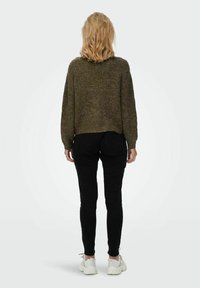 Pull en maille olive cintré avec un tissu texturé, associé à un pantalon slim noir et des sneakers blanches, vu de dos.