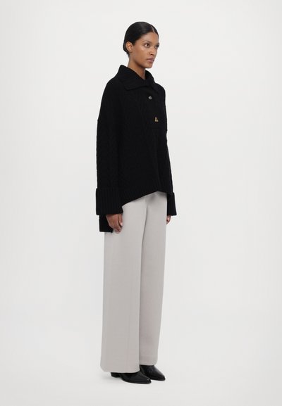 Black knit oversized sweater with a high collar and ribbed cuffs, paired with light gray wide trousers, and black pointed shoes.
