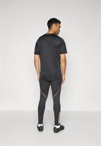 Svart atletisk T-skjorte med korte ermer og sidelommer. Tett sitte svarte leggings med rosa og gule detaljer, og ankelglidelåser.