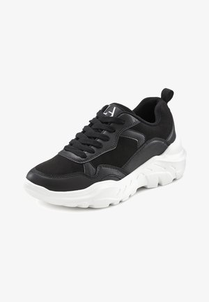 Schwarze Sneaker mit einem Obermaterial aus strukturiertem Leder und Wildleder, ausgestattet mit einer weißen klobigen Sohle, schwarzen Schnürsenkeln und einem kleinen Logo auf der Zunge.