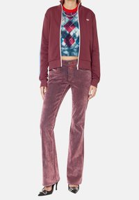 Bordový zipový svetr, zkrácený modrý argyle svetr a růžové kordové kalhoty s rozšířenými nohavicemi. Černé podpatky se stříbrnými akcenty dokončují outfit.