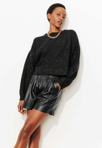 Pull en maille noire avec paillettes argentées, coupe ample. Short en cuir noir avec taille élastique, texture lisse.