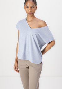 Top azzurro chiaro a maniche corte con un ampio scollo asimmetrico e una consistenza morbida. Abbinato a pantaloni beige, ha una vestibilità rilassata.