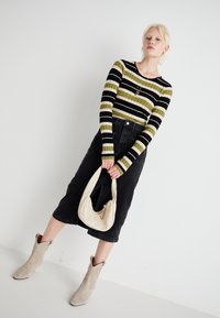 Pull rayé vert et noir en côtes, jupe en denim noire taille haute, sac beigne avec fermeture éclair, et bottines pointues beige clair.