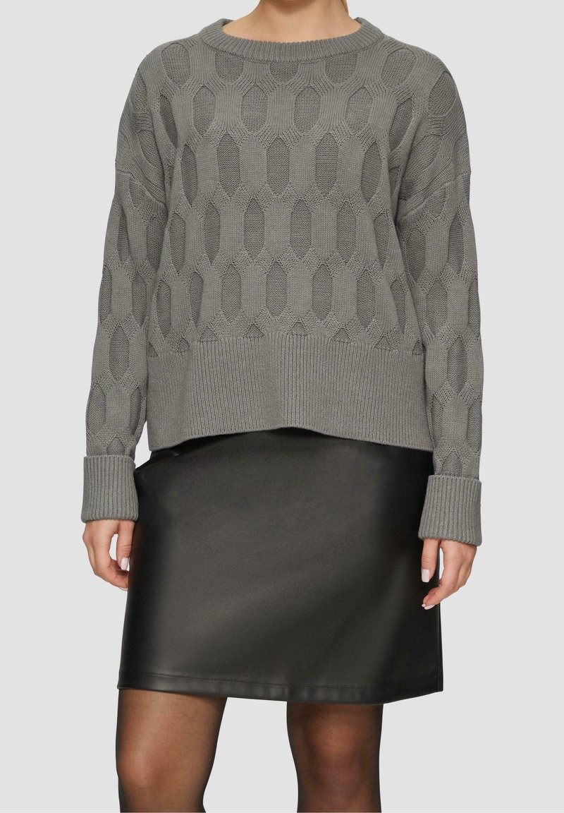 Grå strikket sweater med et struktureret mønster, der har lange ærmer og ribbede manchetter; kombineret med en sort læder miniskørt.
