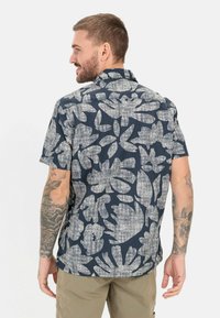 Kurzarmhemd mit dunkelblauem Hintergrund und großem weißen Blumenmuster. Verfügt über einen kragenlosen Ausschnitt und einen entspannten Schnitt.