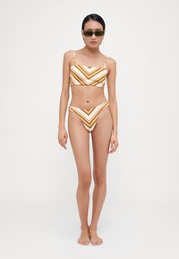 Bikini set s črtami v bež in rjavi barvi, ki vključuje kvadratni crop top in hlačke z visokim izrezom ter chevron vzorcem. Gladka tekstura tkanine.