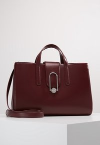 Bordeauxrode leren handtas met twee bovenhandvatten en een afneembare schouderriem. Heeft een metalen sluiting en een gladde textuur.