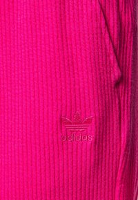 Pink ribbed fabric with a textured surface. Features an embroidered Adidas logo in a matching shade. Side pocket outlined.